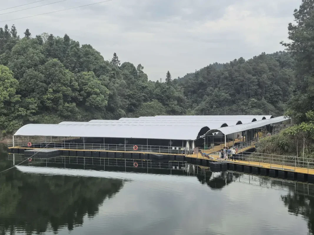 水体和林木覆盖坡地旁的长形顶棚建筑。